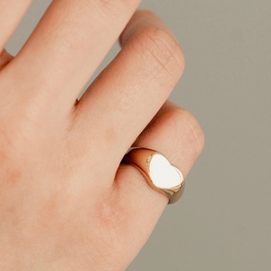 Close-up of a polished gold-plated heart signet ring worn on a finger for a chic look