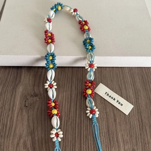 Détail d'un accessoire tressé bohème avec fleurs en perles colorées et coquillages naturels
