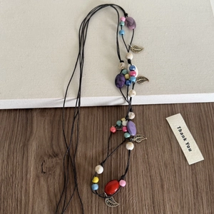 Détail d'un long collier tressé bohème avec perles colorées et pendentifs en bronze