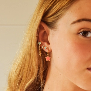 Macro shot of gold moon and star earrings with colorful enamel on a model ear