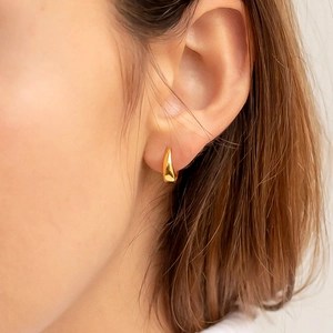 Primo piano dell'orecchino a cerchio huggie dorato lucido indossato per un look lussuoso