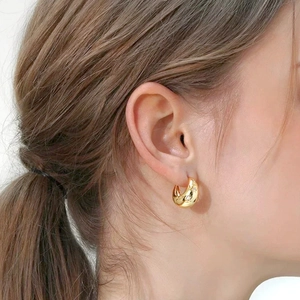 Détail de créoles dorées épaisses avec motifs d'étoiles portées par un mannequin de profil