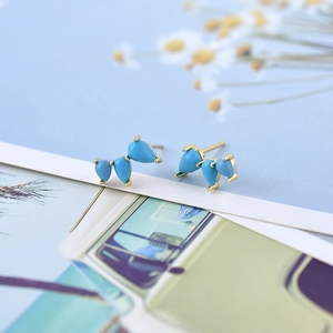 Macro detail of blue wing-shaped stud earrings with gradient zircon on a floral background