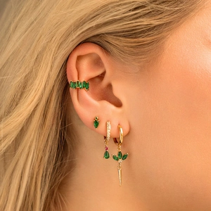 Gold earrings set with green cubic zirconia featuring clover and drop charms on model
