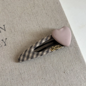 Macro view of checkered fabric hair clip with a pink matte heart and gold lettering