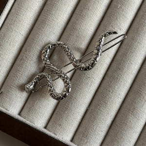 Detailed close-up of a silver snake-shaped hair clip with intricate scale textures