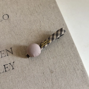 Detail of vintage plaid hair clip with a mauve fabric ball and gold lettering