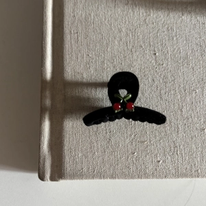 Close-up of a matte black hair clip with red cherry accents on a beige fabric background