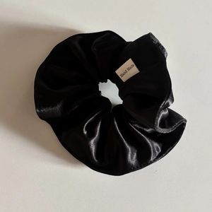 Detail view of black satin scrunchie featuring a white handmade woven label