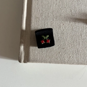 Detailed close-up of cherry stud earrings with red glossy beads and green leaves