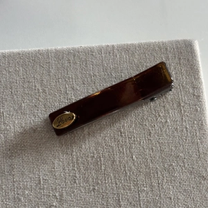 Minimalist amber tortoise shell hair clip with golden Love logo on a beige fabric base