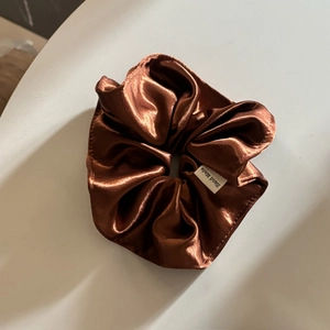 Detail of a brown satin scrunchie showing fabric texture and a Hand Made label tag