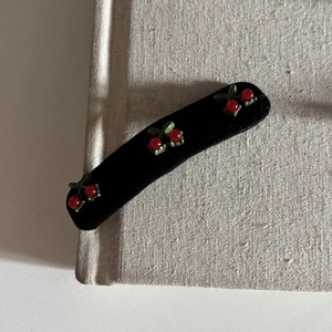 Retro black velvet hair clip with red cherry accents on a minimalist book background