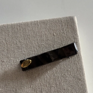 Detailed view of a dark tortoise acetate hair clip featuring a gold Love metal plaque