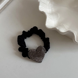 Dettaglio di scrunchie nero con cuore di strass grigio scuro su superficie bianca