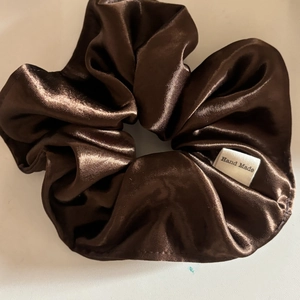 Detailed close-up of a coffee brown satin scrunchie with a Hand Made fabric label