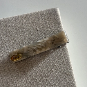 Close-up of beige marble acetate hair clip with gold Love metal tag on linen fabric