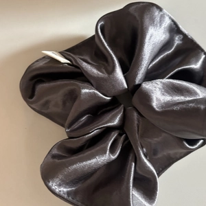 Close-up of a large dark grey satin scrunchie with smooth texture and side label