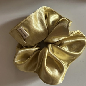 Close-up of golden satin scrunchie featuring a white Hand Made fabric label detail