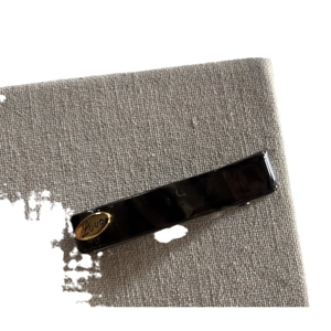 Minimalist black acetate hair clip with vintage gold 'Love' emblem on grey fabric