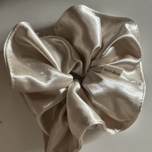 Close-up of champagne satin scrunchie featuring handmade woven label and silky texture
