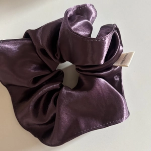 Detail of deep purple satin scrunchie showing glossy fabric texture and Hand Made label