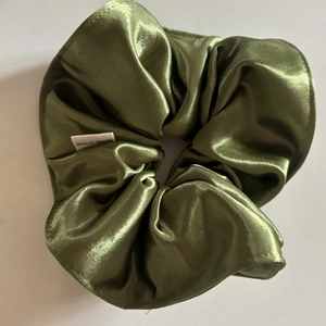 Detailed macro shot of olive green satin scrunchie with a handmade white woven label