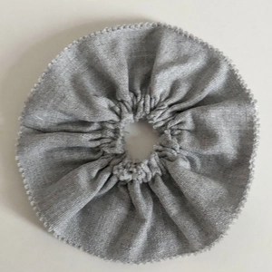 Macro view of a grey pleated suit fabric scrunchie with soft textured cotton blend surface