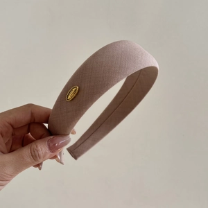 Detailed close-up of pink fabric wide headband with a gold metal plate engraved with Refined Elegance
