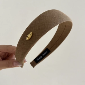 Detail view of brown fabric headband texture with gold metal logo and handmade label