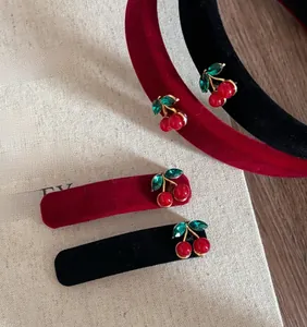 Detailed view of red velvet cherry headband with green gemstone leaf accents on fabric