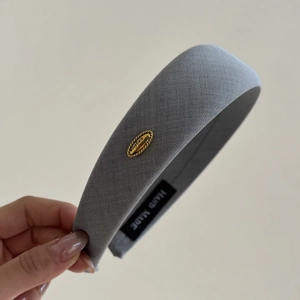Macro shot of grey fabric headband featuring a vintage gold emblem and handmade label