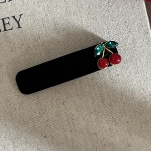 Elegant black velvet cherry hair clip with red beads and green crystals on beige fabric