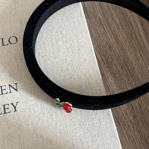 Detailed view of the red cherry charm on a black velvet headband with a retro vibe