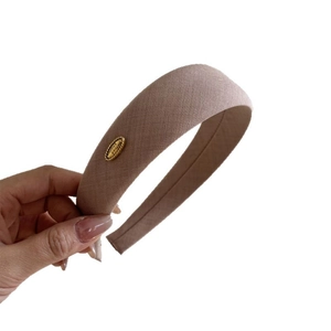 Elegant dusty pink fabric headband with a gold metal tag and twill texture detail