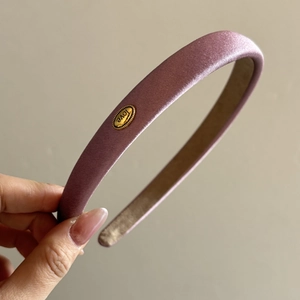 Close-up of pink satin headband featuring a gold oval metal tag engraved with Love text