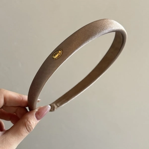 Close-up of champagne silk headband featuring a golden oval metal plate with Love engraving