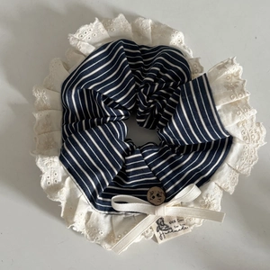 Détail d'un chouchou rayé bleu marine avec bordure dentelle, nœud et bouton en bois