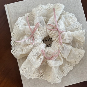 Detailed texture of cream lace scrunchie featuring pink ribbon bows on linen book cover