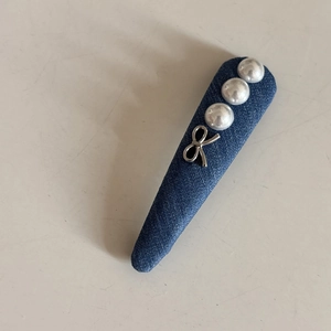 Détail d'une pince à cheveux en denim ornée de trois perles blanches et d'un nœud argenté