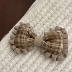 Close-up of brown plaid bow hair clip with wavy pleated lace trim on a cozy knit background