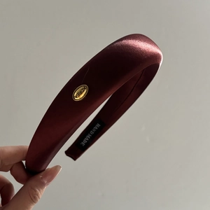 Detail view of burgundy satin padded headband with gold KOREA tag and handmade label