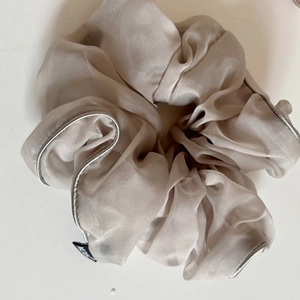 Detail of organza scrunchie with silver stitching and brand label in champagne color