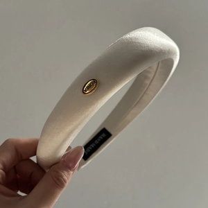 Detail of a padded cream satin headband with a gold-tone metal Korea logo plate