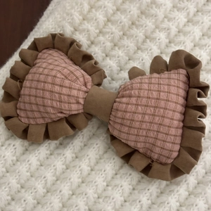 Detail of pink plaid bow hair clip with brown ruffled edges on white knit background