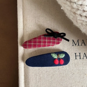 Detail of fabric bow hair clips with cherry embroidery on a textured book surface
