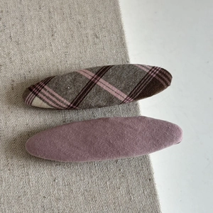 Detail of plaid fabric bow and mauve pink snap hair clip set on neutral texture