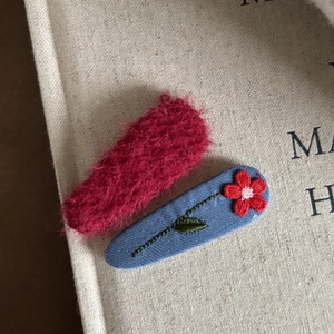 Detail of red floral embroidery on blue fabric clip and pink plush hair accessory