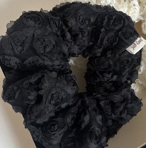 Detailed close-up of a black lace scrunchie with a 3D rose flower and white brand label