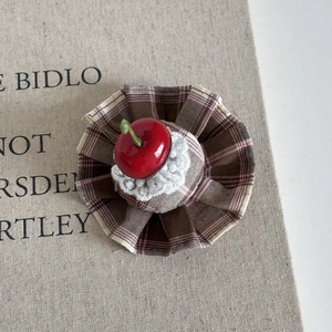 Detailed macro view of a cherry hair clip with lace and brown plaid fabric base
